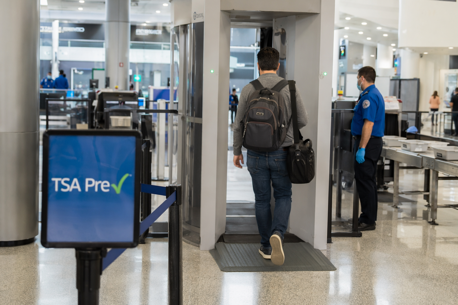 Traveler using a TSA PreCheck lane at an airport security checkpoint with shoes on and a laptop bag over the shoulder
